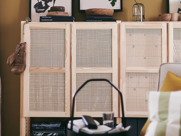 In a living room are two IVAR cabinets in natural pine with bamboo weave doors. Books, and deco objects are on top of them.