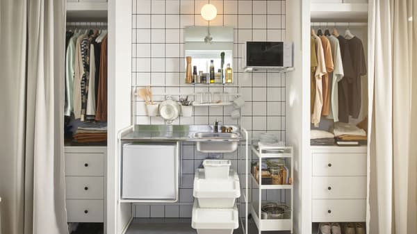 In a shared dorm room, a SUNNERSTA mini kitchen is sandwiched between two closets. Curtains hang in front of the closets.