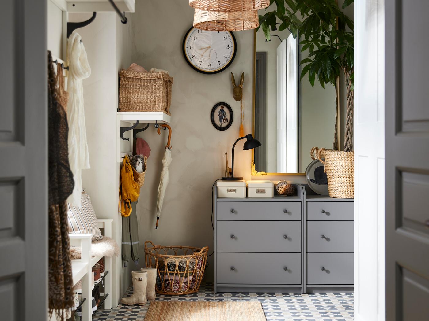 In een hal staan twee grijze PLATSA ladekasten naast een SNIDAD mand vol textiel. Aan de muur hangt een KUTTERSMYCKE klok.