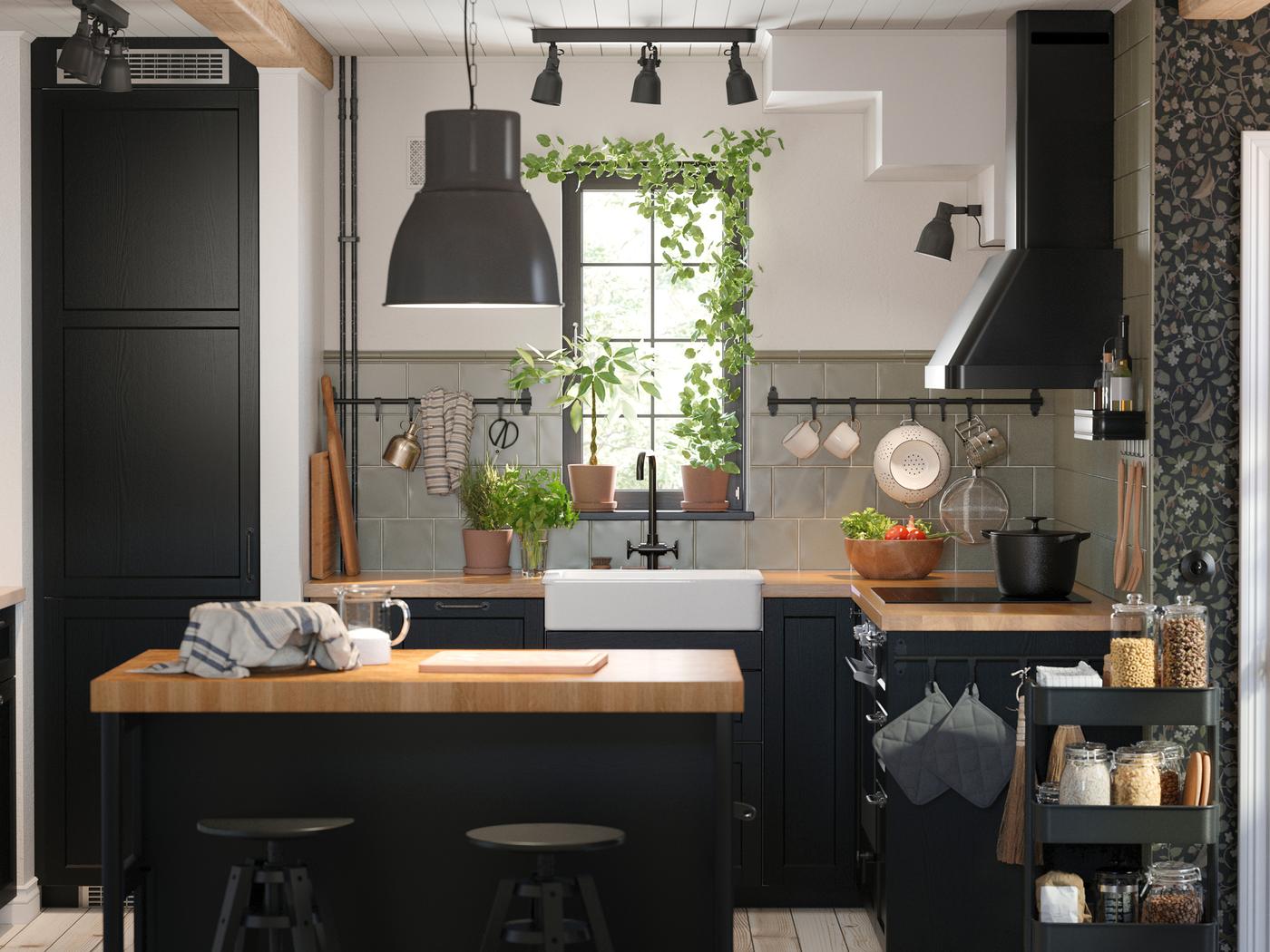 In een keuken met zwart gebeitste LERHYTTAN fronten staat een keukeneiland met een houten werkblad en hierboven een zwarte hanglamp.