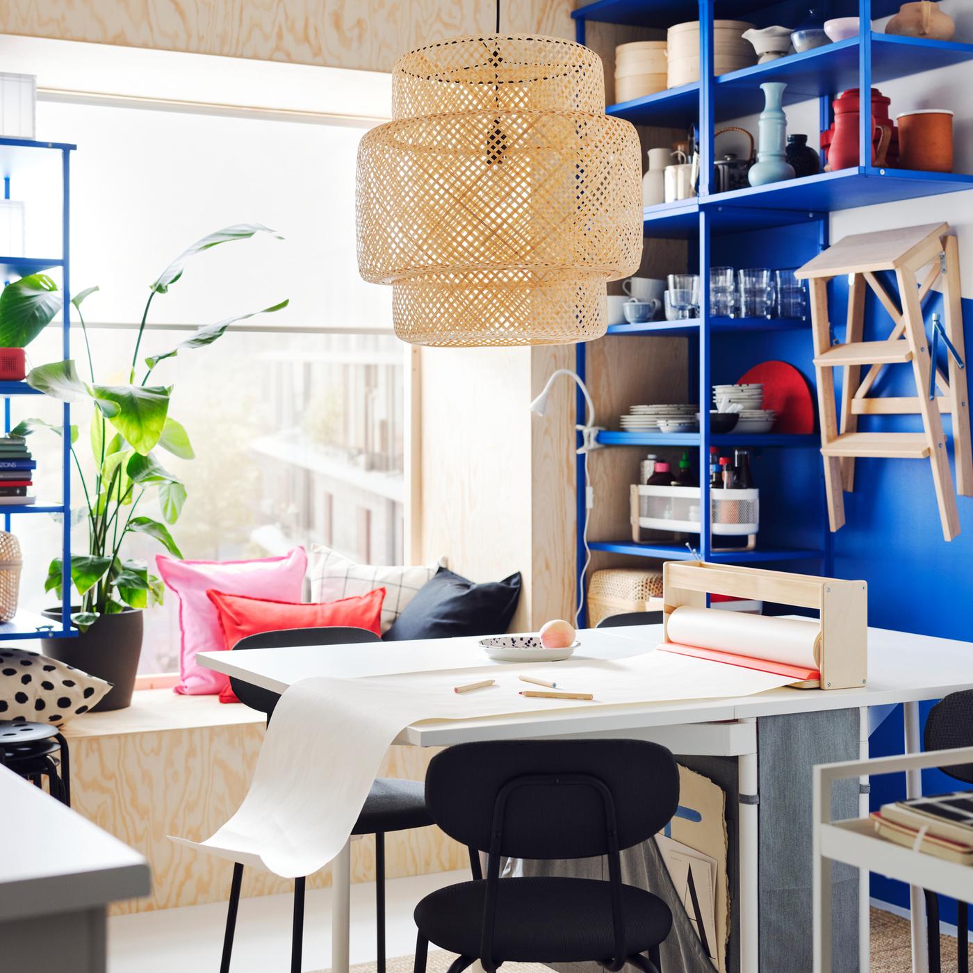 In een kleurrijke eetkamer in Scandinavische stijl staat een klaptafel met opberger en tegen de blauwe muren staan blauwe PLATSA open stellingkasten.