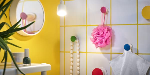 In einem Badezimmer sind bunte Kacken montiert an denen ein Schwamm und Handtücher hängen.