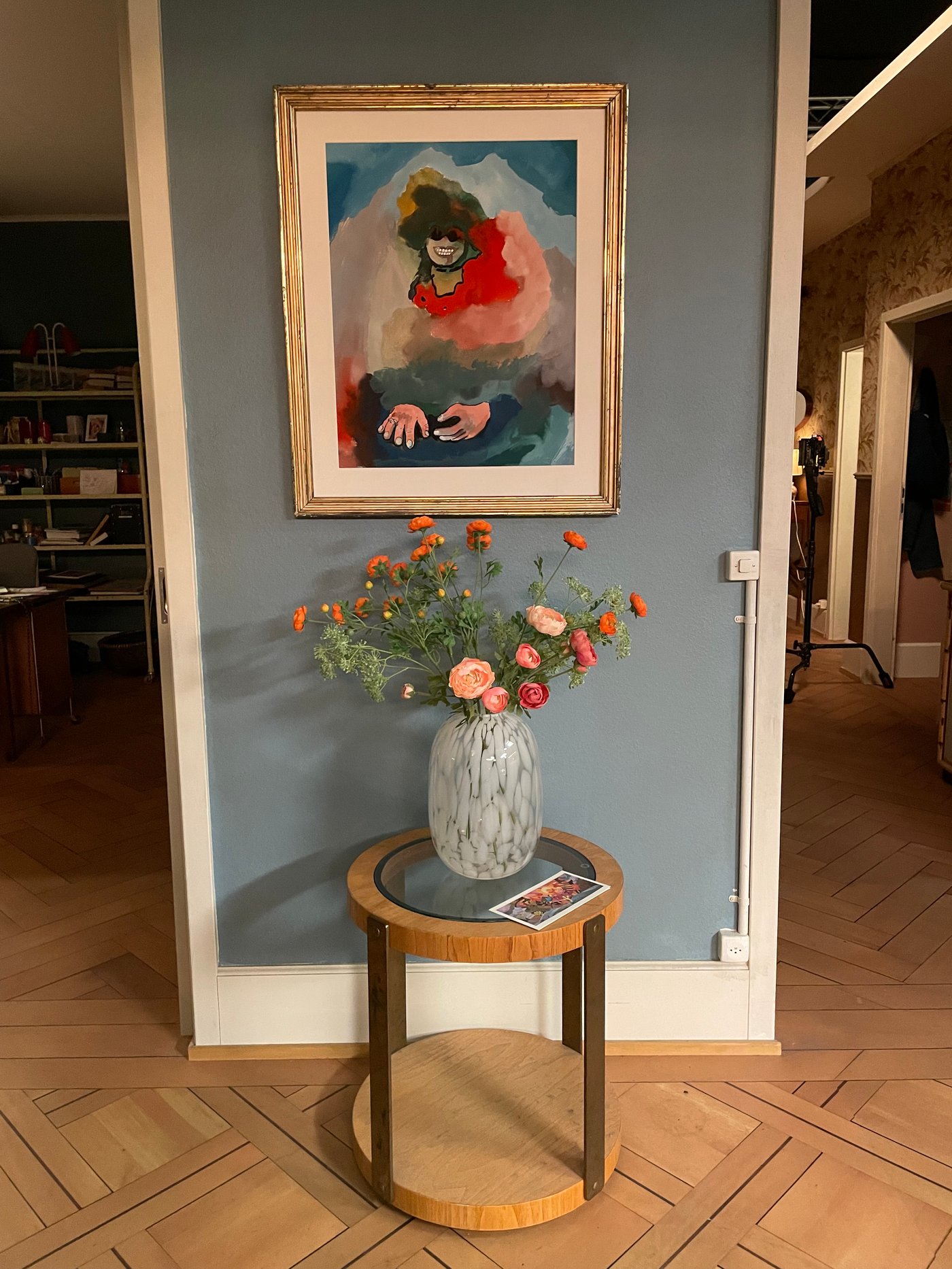 In einem Flur steht ein kleiner Beistelltisch an einer Wand mit einer Blumenvase darauf. Dahinter hngt ein Bild mit goldenem Rahmen an der Wand.