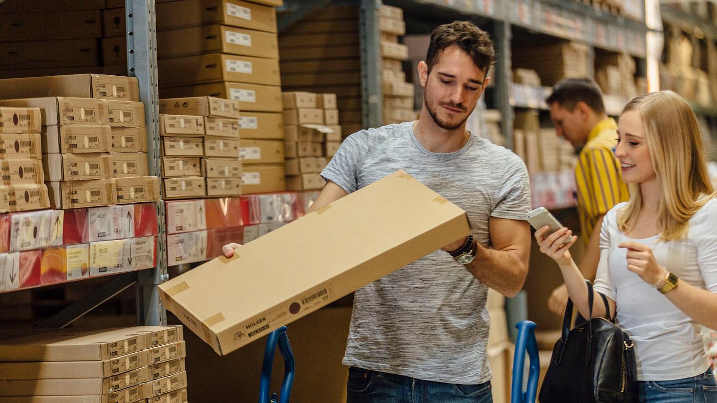In einem IKEA Einrichtungshaus stehen zwei Kunden und scannen ein Produkt in der Markthalle mit dem Smartphone.