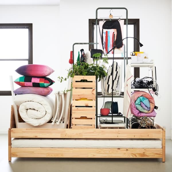 In einem Raum stehen viele Ikea Holzboxen neben einem Kleiderständer auf dem bunte Kleidung hängt
