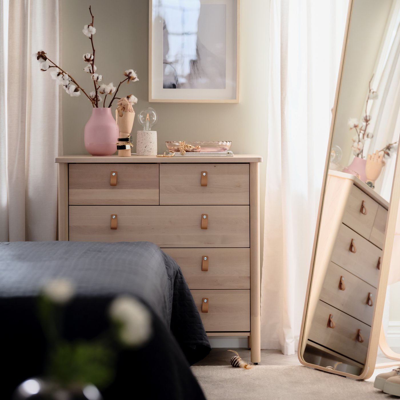 In einem Schlafzimmer ist eine BJÖRKSNÄS Kommode mit 5 Schubladen in Birke zu sehen, auf der sich dekorative Gegenstände befinden. Daneben steht ein IKORNNES Standspiegel aus Esche.