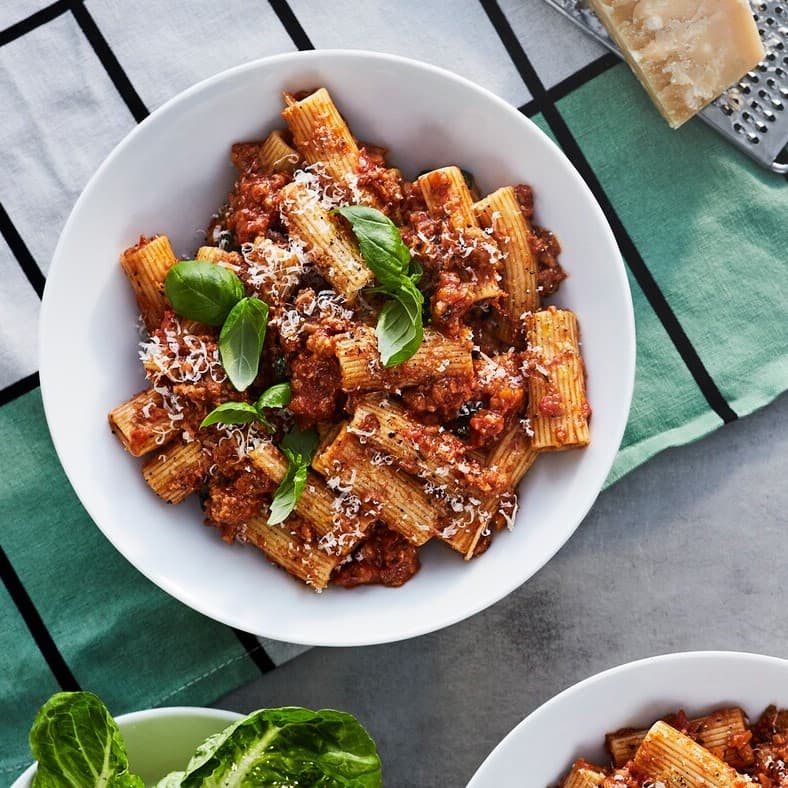 In einer weißen Schüssel liegt eine pflanzliche Bolognese mit Basilikum oben drauf