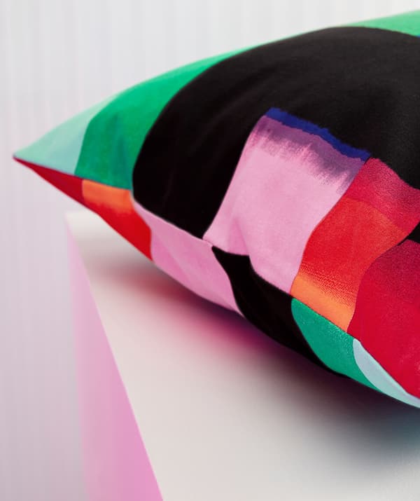 În prim-plan, o pernă decorativă cu imprimeu multicolor.