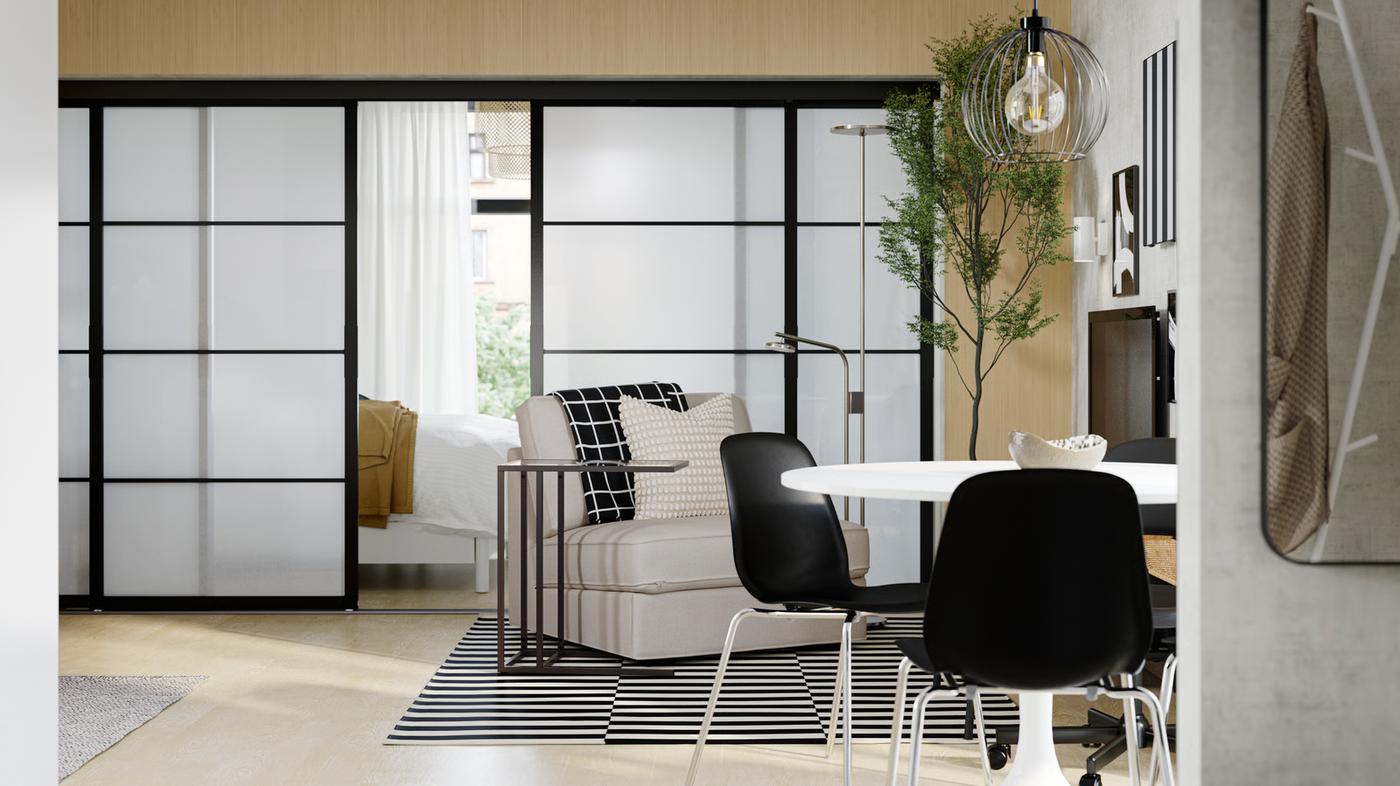 In un appartamento arioso e minimalista, un open space con zona pranzo e soggiorno di fronte a porte scorrevoli SKYTTA che delimitano una camera da letto.