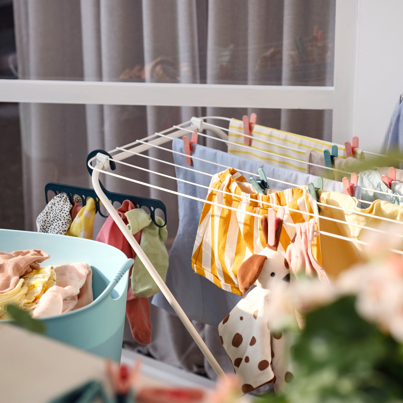 In un balcone, uno stendibiancheria da interno/esterno FROST bianco a cui sono appesi vestiti di colori diversi - IKEA. 