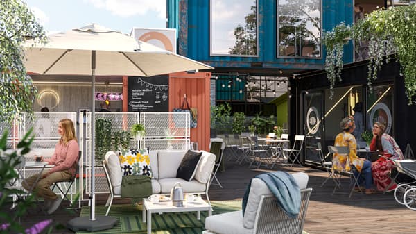 In un villaggio di container, un'area lounge all'aperto con il sole che splende. Alcune persone chiacchierano, sedute attorno a tavoli SUNDSÖ grigi - IKEA.