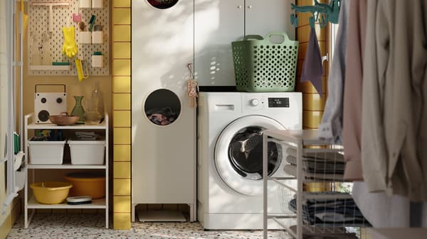 In una lavanderia con piastrelle gialle, un mobile NYSJÖN bianco con una lavatrice bianca e accessori in diversi colori - IKEA.