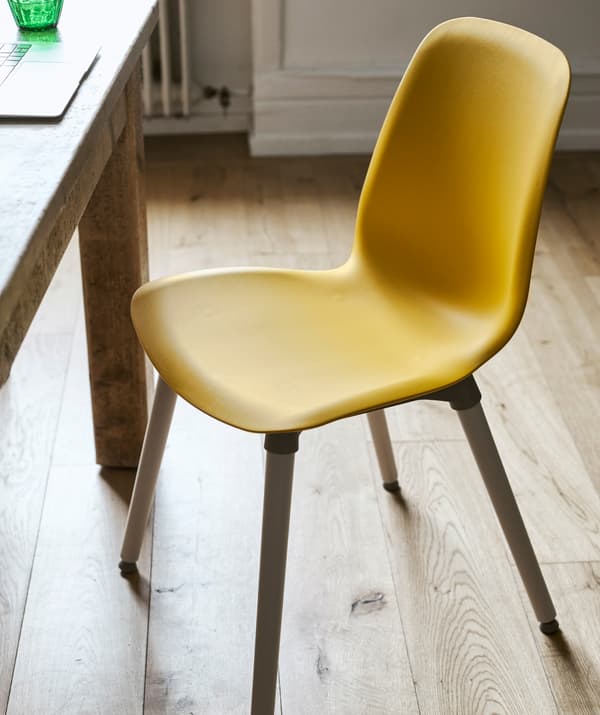 In una stanza con pavimento in parquet, una sedia dal sedile in plastica giallo scuro e gambe in legno, accanto a un tavolo in legno.