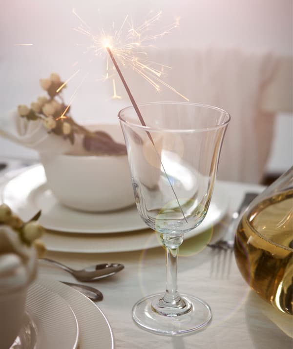 Individual place at extravagantly set table, white tableware and flowers, fronted by a wine glass holding a lit sparkler.