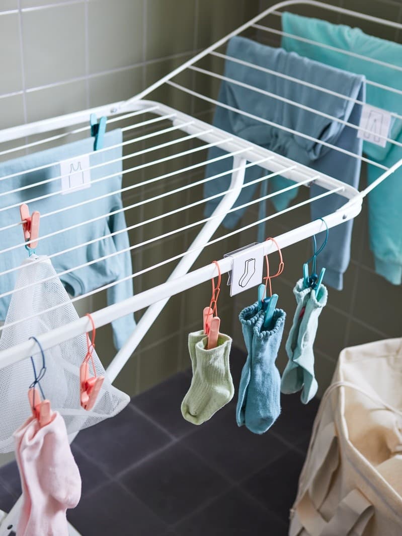 Indoor drying rack with colorful clothes hanging on clothespins in a tiled laundry area.