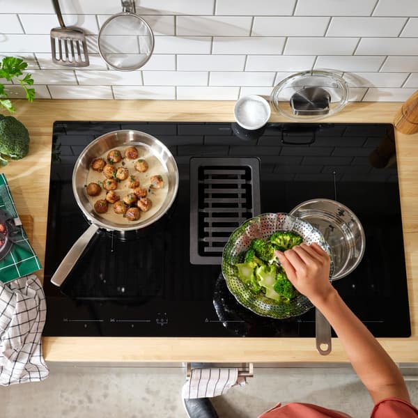 Indukčná varná doska so zabudovaným odsávačom, na ktorej je položená brokolica a mäsové guľôčky.