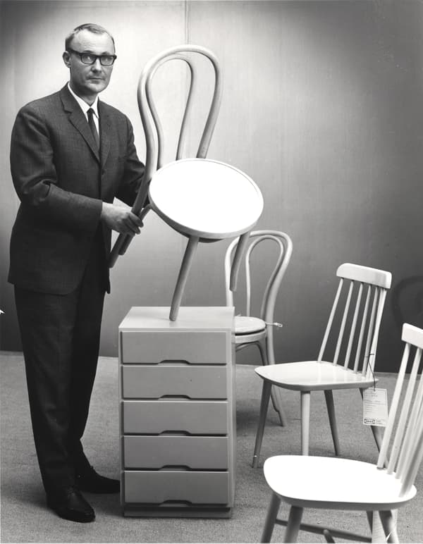 Ingvar Kamprad holding a dining chair next to other chairs, in a black and white photo.