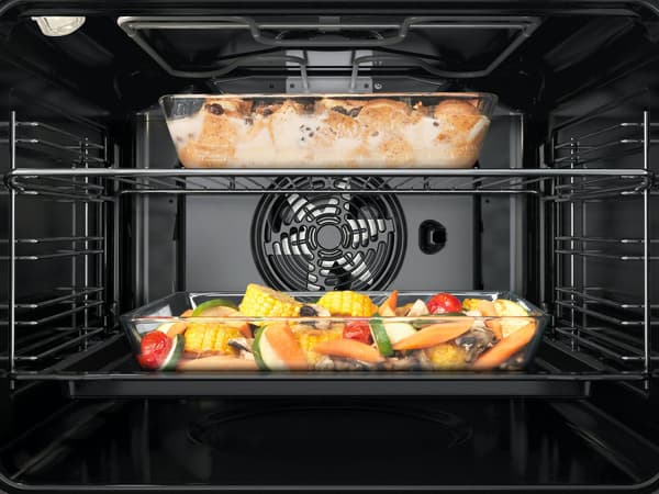 Innenansicht eines Backofens mit zwei Blechen: Oben ein gebackenes Gericht, vermutlich Brot oder Gebäck; unten verschiedenes Gemüse wie Paprika und Zucchini, zum Rösten angerichtet.