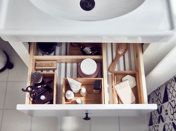 Innsiden av den øverste skuffen i et servantskap, der baderomstilbehør ligger i et DRAGAN oppbevaringssett i fire deler i bambus.