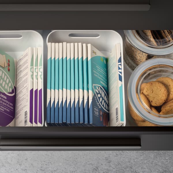 Inside of a kitchen drawer filled with chocolate bars organised in white boxes and glass jars with biscuits.