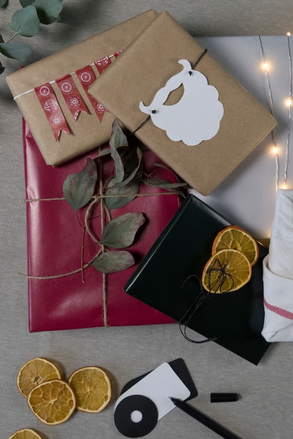 Inslagna paket i olika presentpapper och med olika snören och pynt, i en hög på en duk.