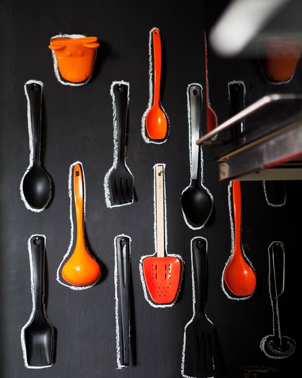 Instead of hiding utensils away, here they’re on display. Bright orange utensils hang on a black chalkboard background.