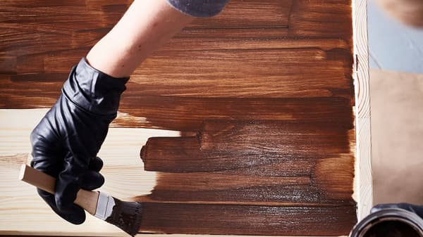 Interiérová designérka v černých latexových rukavicích natírá mořidlem komodu IKEA RAST na tmavě hnědou.