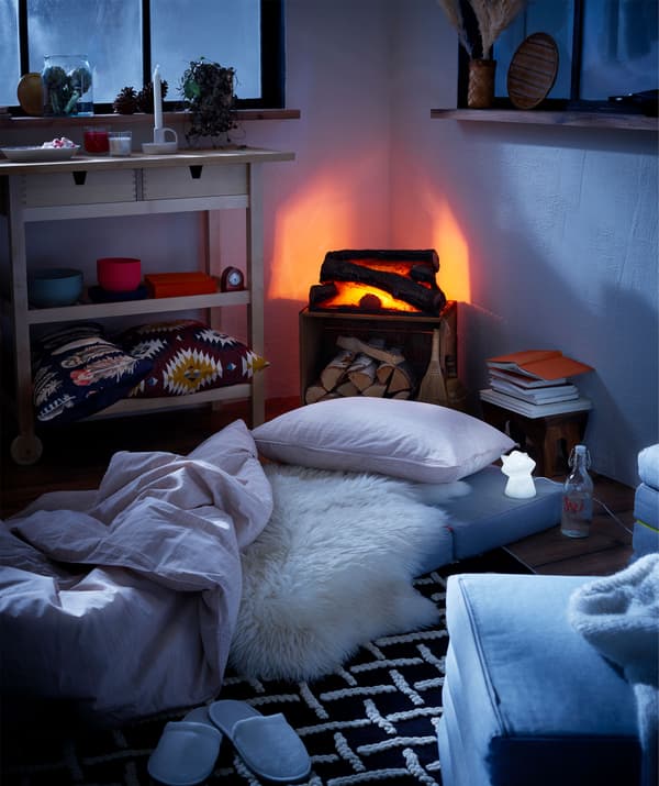 Intérieur de type maisonnette avec faux feu de bois et matelas sur le sol comme lits temporaires, veilleuses LED à côté.