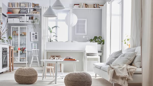 Intérieur d’un studio dans une palette de tons clairs: lit, canapé, kitchenette, rangements, et deux poufs SANDARED.