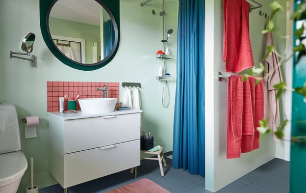 Intérieur d’une salle de bains bien organisée aux tons pastel avec meuble-lavabo, douche, porte-serviettes, miroir, plantes et accessoires.