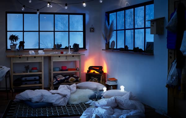 Interior de estilo cabana de inverno, colchóns no chan a xeito de camas temporais e luces LED de noite ao seu carón.