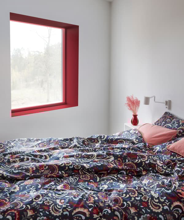 Interior de um quarto e uma cama com roupa de cama em cores vivas e decorada com um padrão sueco tradicional com cornucópias.