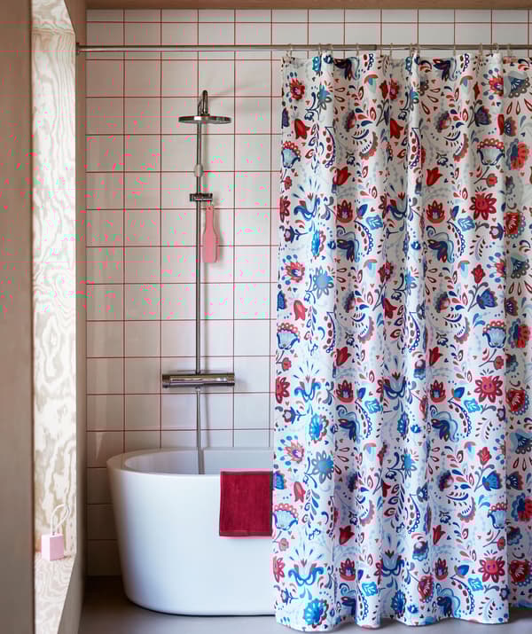 Interior de uma casa de banho com uma cortina de duche com um padrão elaborado pendurada em frente a uma banheira com chuveiro.