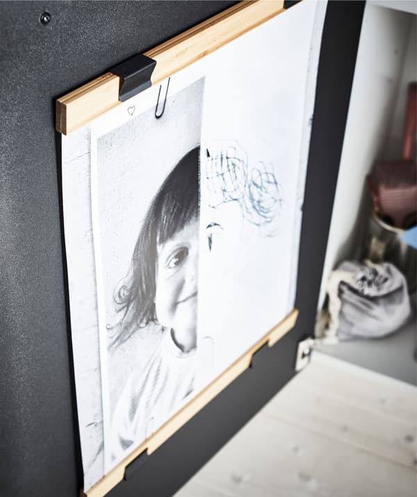 Interior de un armario de cocina con dos soportes de póster (uno arriba y otro abajo) mostrando la obra de un joven artista.