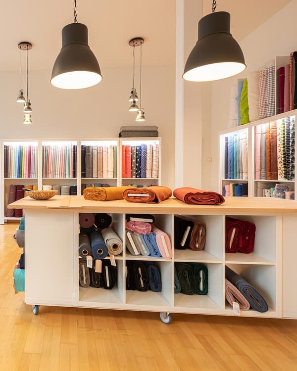 Interior view of a fabric shop with a large tailoring table in the centre and lots of shelves holding fabrics
