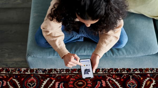 青いソファに座り、スマートフォンを操作する人物。足元に赤い柄のラグが敷かれている。