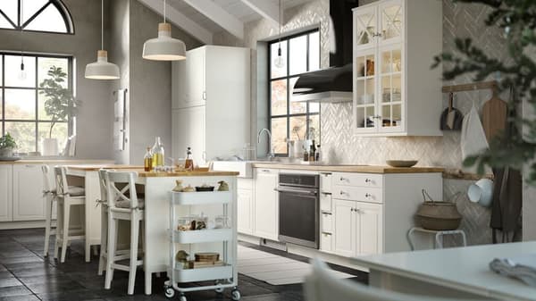 It is a bright kitchen in a white style. There is a kitchen island with chairs on the side and an oven in the center.