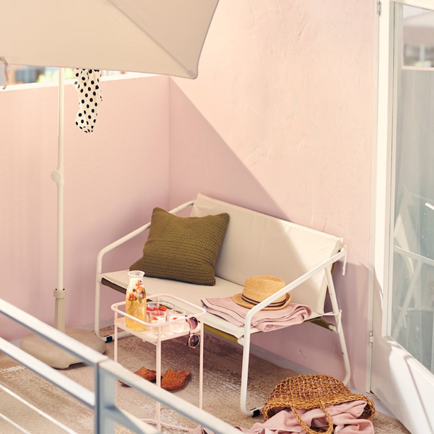 It’s a sunny afternoon on this urban balcony with white outdoor furniture, including a two-seat sofa and parasol.