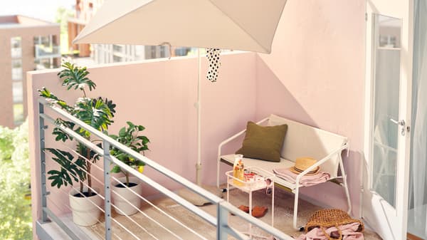 It’s a sunny afternoon on this urban balcony with white outdoor furniture, including a two-seat sofa and parasol.