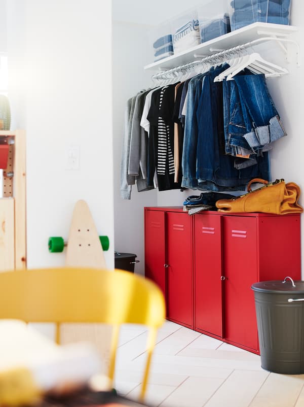 ส่วนของผนังที่มีตู้เสื้อผ้าและที่เก็บของบนโถงทางเดินรวมกัน: ตู้ IVAR/อิวาร์ สีแดงอยู้ใต้เสื้อที่แขวนเรียงเป็นแถวอยู่บนราว