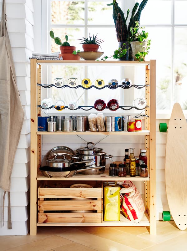 ชั้นวาง IVAR/อิวาร์ ตั้งอยู่ข้างหน้าต่าง จัดไว้เหมือนห้องเตรียมอาหารขนาดเล็ก มีหม้อ ของแห้ง อาหารกระป๋อง และขวดอยู่บนชั้น