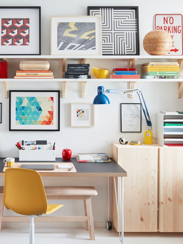 โต๊ะมีล้อตั้งอยู่ข้างผนัง ล้อมรอบด้วยตู้ IVAR/อิวาร์ ไม้สีอ่อน ชั้นแขวนผนัง และงานศิลปะในกรอบ