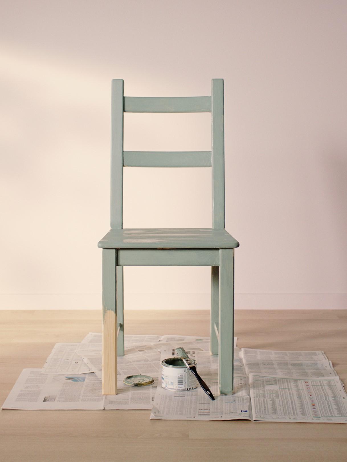 IVAR chair painted light green standing on old news papers in an empty room with light wooden floor and light pink walls.