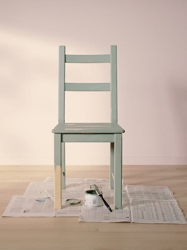 IVAR chair painted light green standing on old news papers in an empty room with light wooden floor and light pink walls.