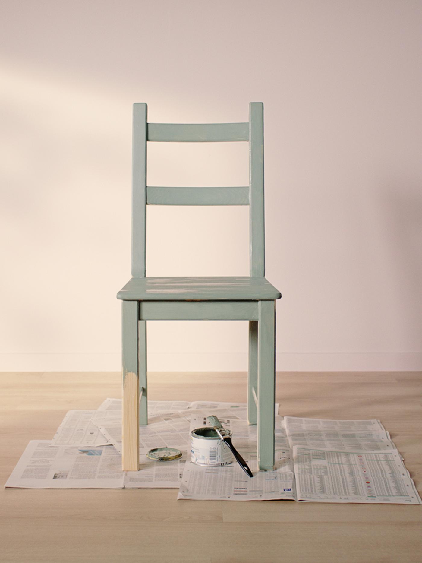 IVAR chair painted light green standing on old news papers in an empty room with light wooden floor and light pink walls.