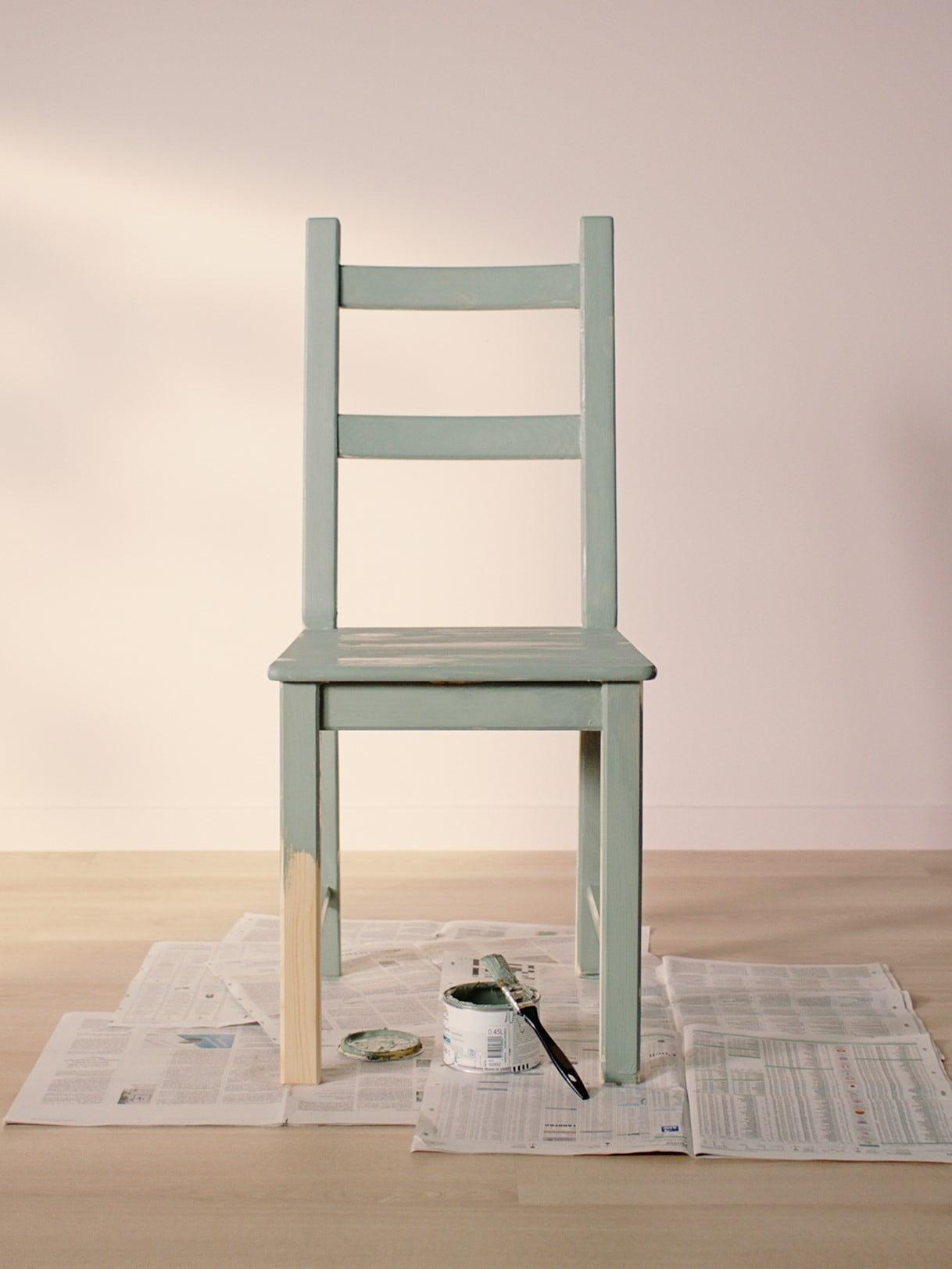 IVAR chair painted light green standing on old news papers in an empty room with light wooden floor and light pink walls.