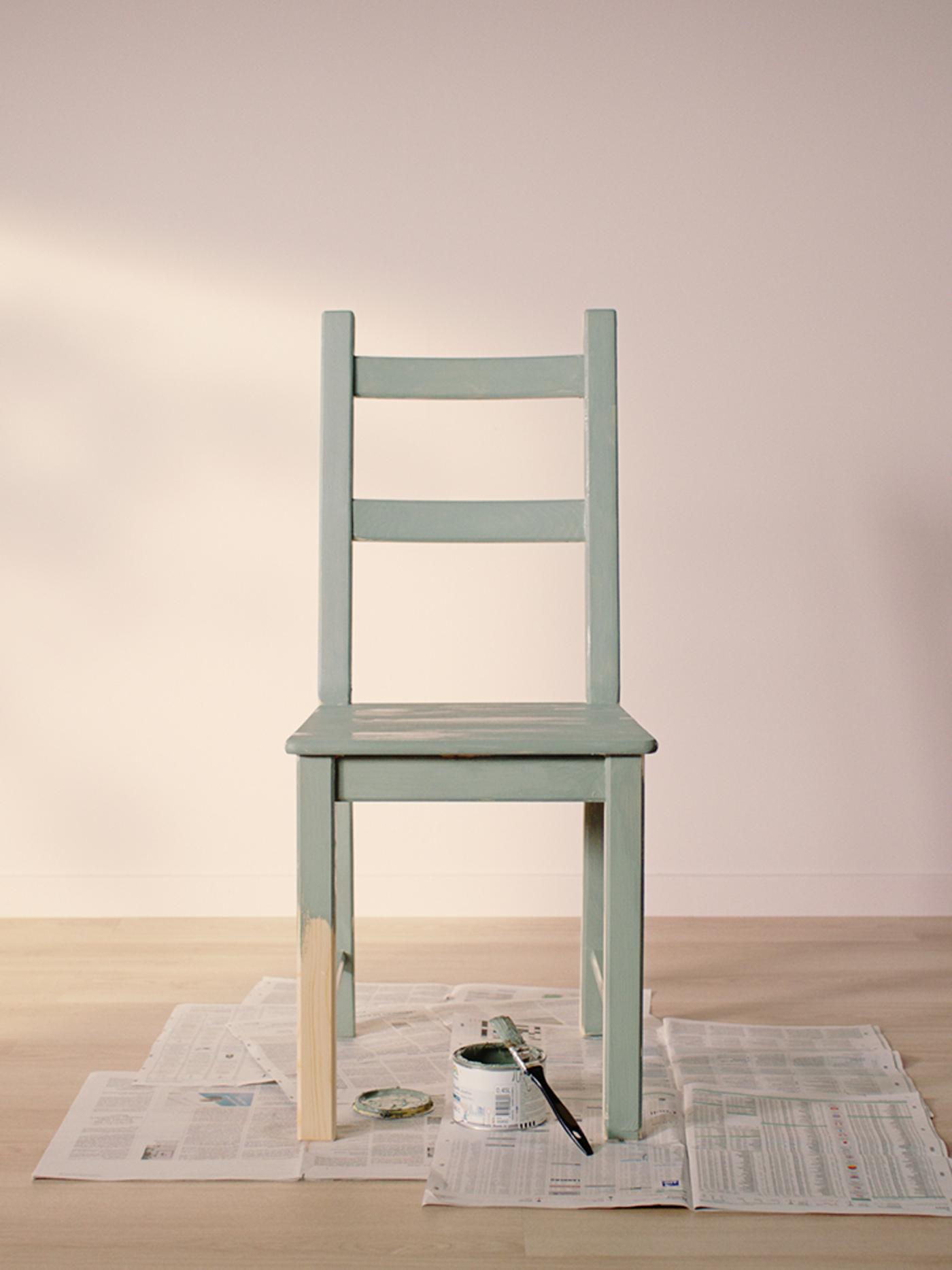 IVAR chair painted light green standing on old news papers in an empty room with light wooden floor and light pink walls.