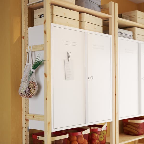 IVAR white metal cabinets on shelf sections in pine and a metal clip with a note is placed on the metal door of the cabinet.