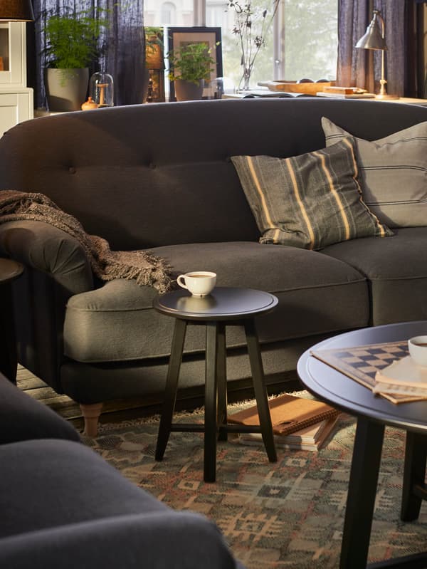 Izba s tmavosivou pohovkou ESSEBODA, v popredí sú dva čierne okrúhle stolíky KRAGSTA.