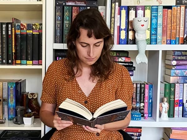 Jacqui liest ein Buch vor ihrem Bücherregal.